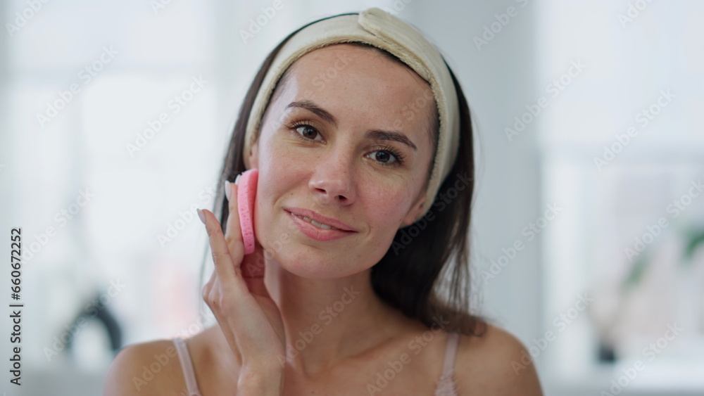 Smiling woman cleaning face looking camera pov view. Happy girl using sponge
