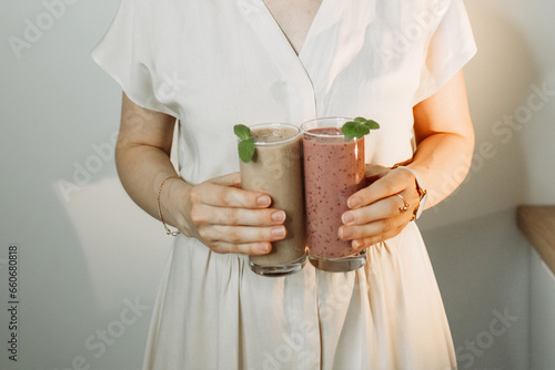 A woman holds a smoothie with green spinach, pistachios and a blueberry cocktail in her hands.