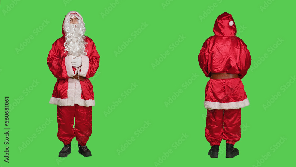 Fototapeta premium Man acting like santa in costume saying ho ho ho, portraying december famous character for christmas eve celebration. Saint nick with hat and beard standing over full body greenscreen.