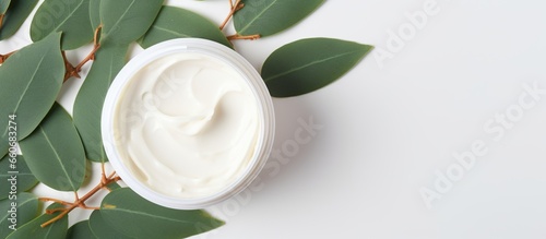 A white cosmetic jar with natural facial cream on white background next to leaves photo