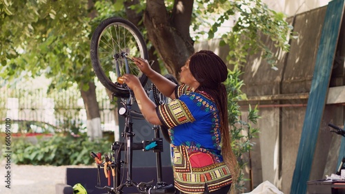 Motivated black woman fine-tuning bicycle tire in home yard with an assortment of professional tools. Young african american lady realigning and securing bike wheel for summer leisure cycling.