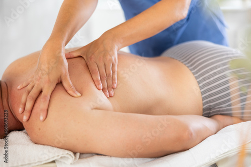 The masseur makes a massage on the shoulders of a man who lies on the couch