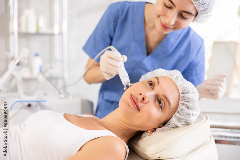 Young woman receiving facial radiofrequency procedure stimulating collagen production resulting in tightened and firmed skin. Modern hardware cosmetology