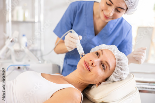 Young woman receiving facial radiofrequency procedure stimulating collagen production resulting in tightened and firmed skin. Modern hardware cosmetology