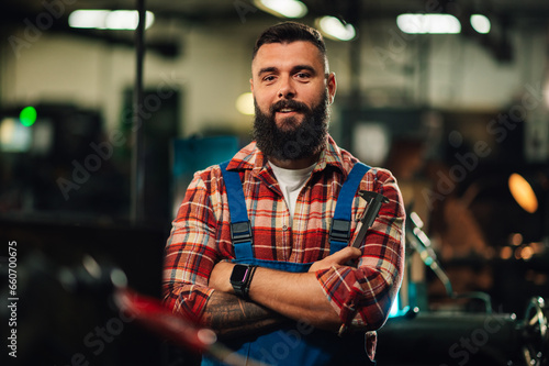 Obraz na płótnie Portrait of a young factory worker, crossed tattooed arms, holding a caliper