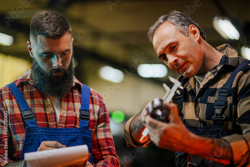 A mechanical engineer examining and measuring a metal part with his assistant.