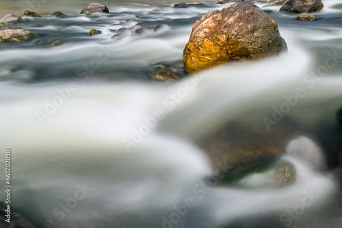 Stone in the midle of the river. Slow motion river water flows around the stone.