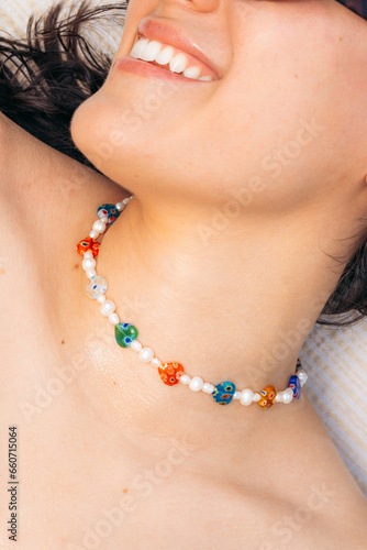 Close-up view of an anonymous white girl with a big smile wearing a pearl necklace and colorful hearts during a sunny day