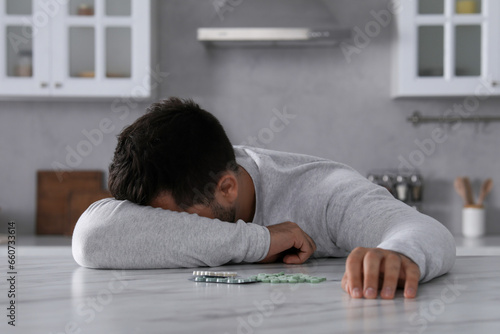 Принти на полотні Man with antidepressant pills sleeping at white marble table in kitchen
