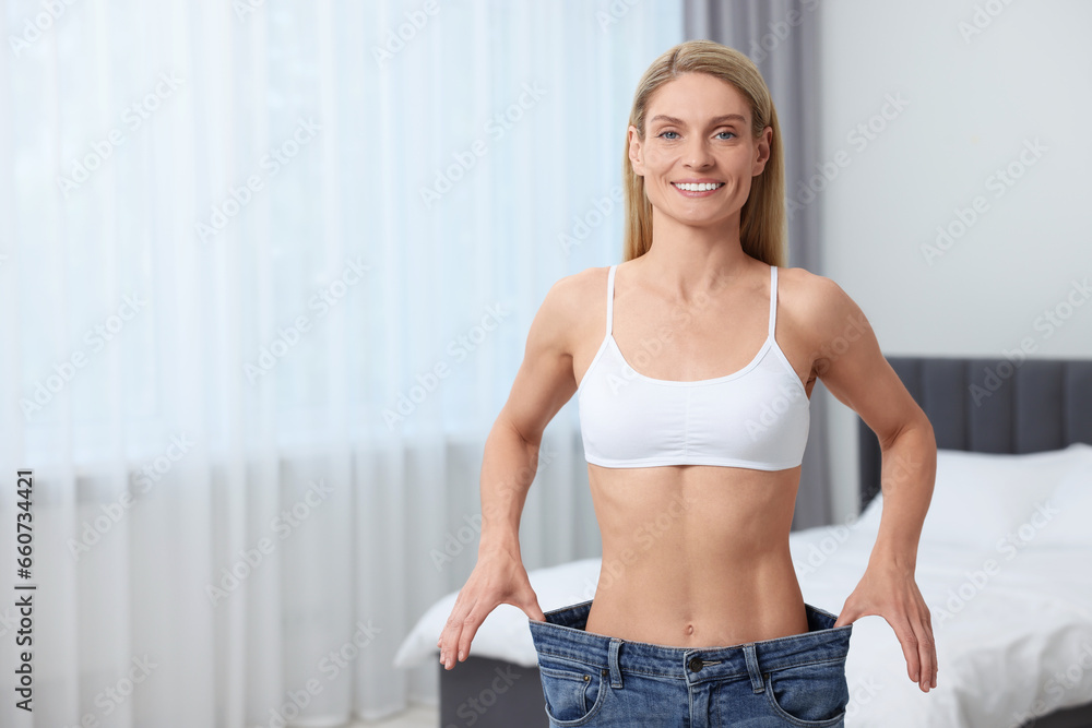 Slim woman wearing big jeans at home, space for text. Weight loss