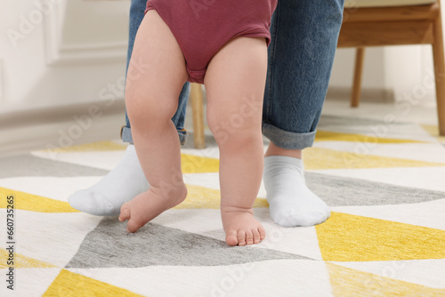 Mother supporting her baby son while he learning to walk on carpet at home  closeup