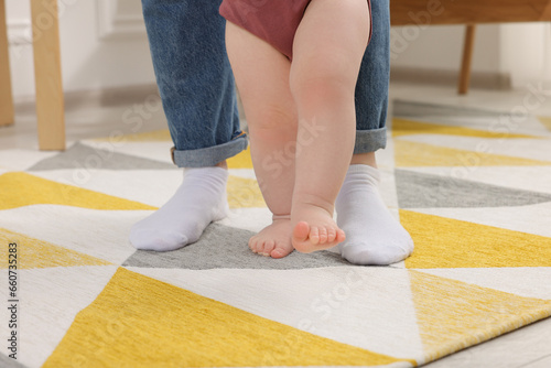 Mother supporting her baby son while he learning to walk on carpet at home, closeup