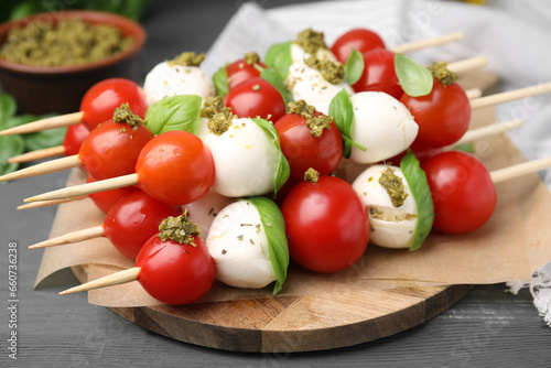 Caprese skewers with tomatoes, mozzarella balls, basil and pesto sauce on grey wooden table, closeup