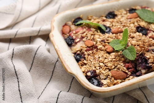 Tasty baked oatmeal with berries and almonds in baking tray on tablecloth, closeup. Space for text