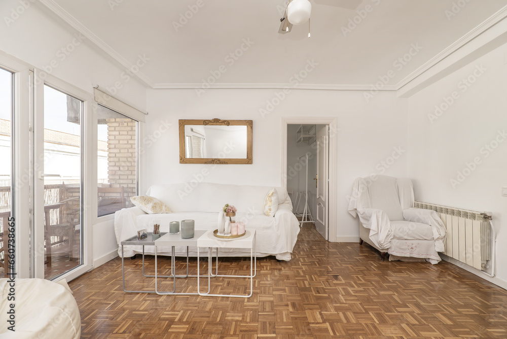 Large living room of an apartment with some white furniture, white lacquered glass access doors, oak parquet floor with checkerboard slats and access to the terrace through white aluminum glass Large living room of an apartment with some white furniture, white lacquered glass access doors, oak parquet floor with checkerboard slats and access to the terrace through white aluminum glass