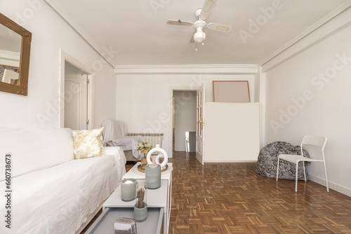 Large living room of an apartment with some white furniture  white lacquered glass access doors  oak parquet floor with checkerboard slats and matching decorative objects