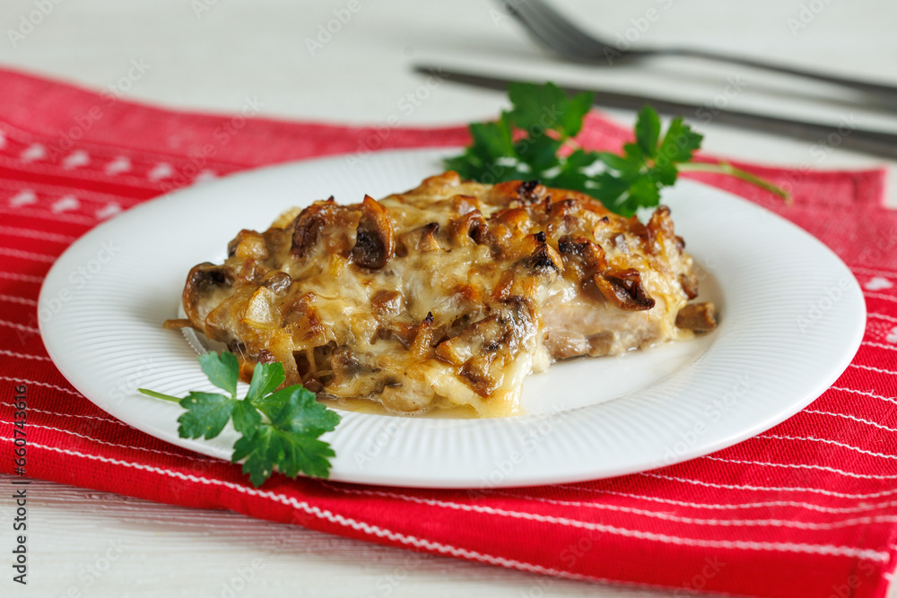 homemade baked chicken fillet steak with mushrooms and cheese on plate on red napkin on white wooden table. Party menu homemade baked chicken fillet steak with mushrooms and cheese on plate on red napkin on white wooden table. Party menu