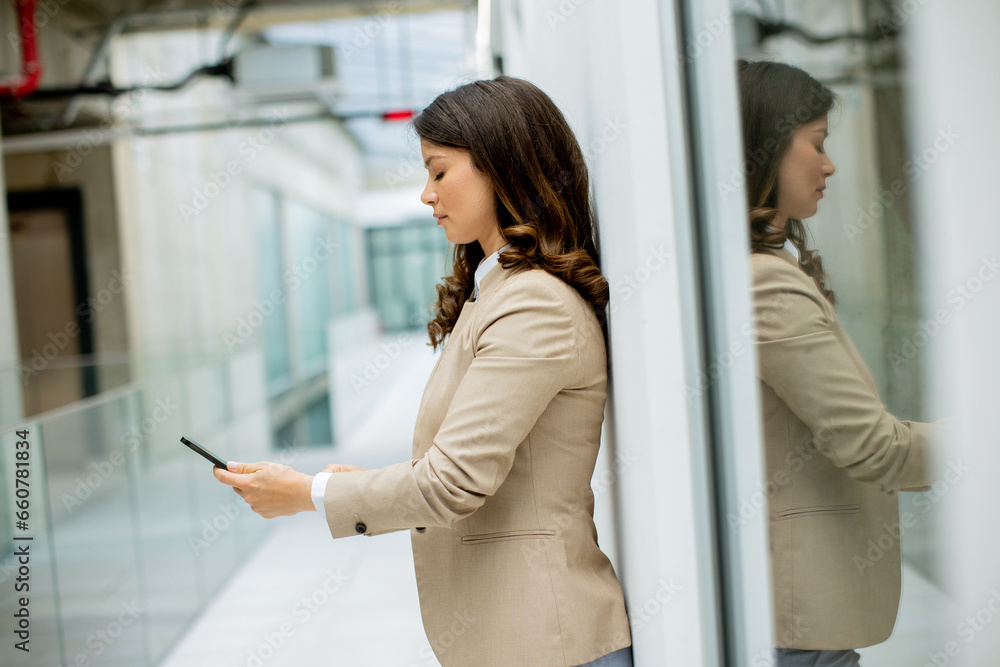 Fototapeta premium Young business woman using mobile phone in the office hallway