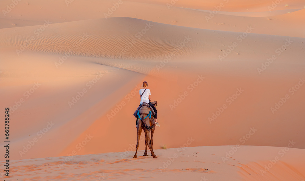 General view of the Merzouga hotels district with full moon - Merzouga, Sahara, Morocco   - A woman riding a camel across the thin sand dunes of the in Western Sahara Desert - Morocco