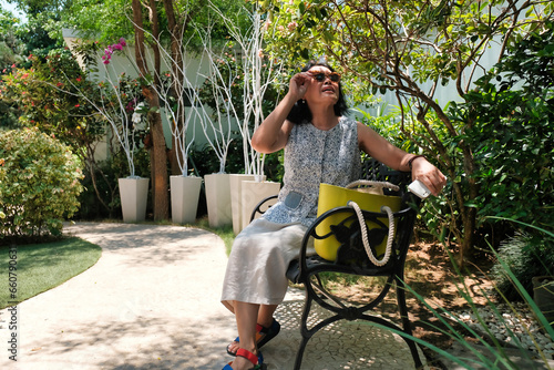 A housewife wearing sunglasses, sitting in the home garden under hot sunny day photo