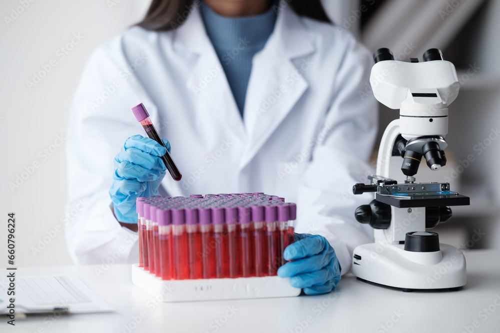 Doctor hand taking a blood sample tube from a rack with machines of analysis in the lab background, Technician holding blood tube test in the research laboratory. Doctor hand taking a blood sample tube from a rack with machines of analysis in the lab background, Technician holding blood tube test in the research laboratory.