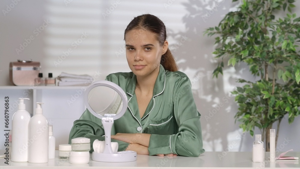 Portrait of a woman without makeup in green pajamas. Woman sitting at dressing table with cosmetic bottles. Portrait of a woman without makeup in green pajamas. Woman sitting at dressing table with cosmetic bottles.