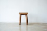 a single, wooden stool against a white wall