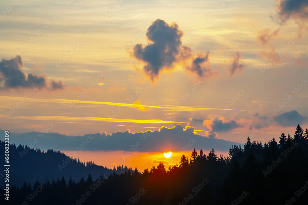 Fototapeta premium Colorful clouds in the sky at sunset against the backdrop of a mountainous forest area.