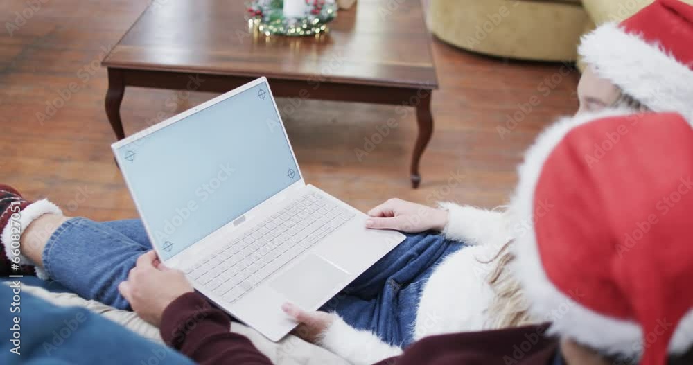 Diverse couple wearing santa hats using laptop with copy space on screen, in slow motion Diverse couple wearing santa hats using laptop with copy space on screen, in slow motion