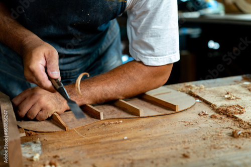 Fotografie Close-up of guitar luthier using chisel to shave bracing of acoustic guitar