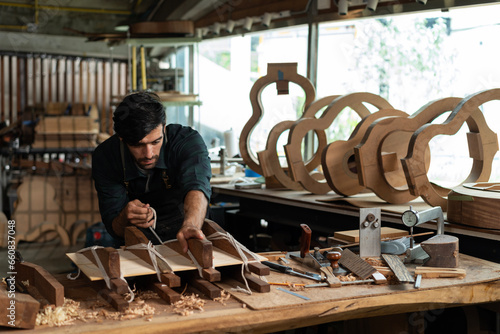 Fotografie Guitar luthier ties rope, drives wedge to join spruce wood boards