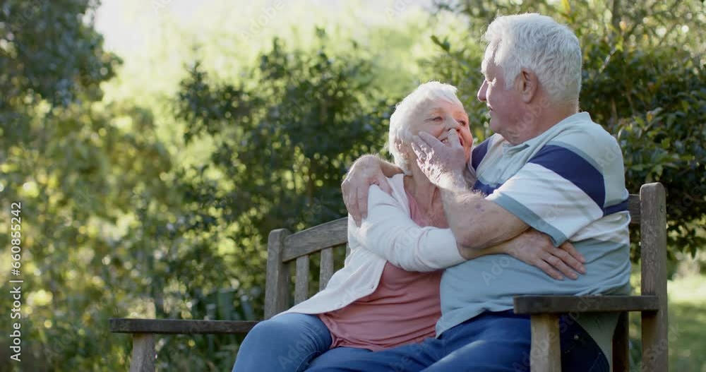 Happy senior caucasian couple sitting on bench embracing in sunny garden, slow motion Happy senior caucasian couple sitting on bench embracing in sunny garden, slow motion