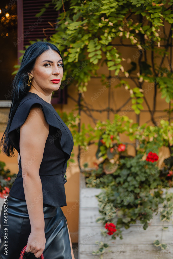 Beautiful woman with dark hair and red lips walking on background of ancient building covered with green climbing plants. Elegant lady in stylish attire exploring old European city. Copy space. Beautiful woman with dark hair and red lips walking on background of ancient building covered with green climbing plants. Elegant lady in stylish attire exploring old European city. Copy space.