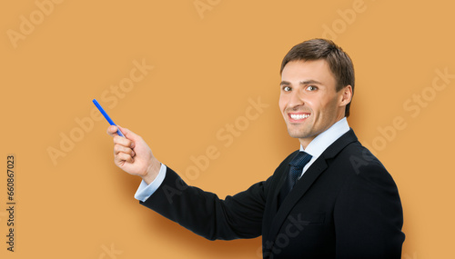 Image of business man in black confident suit, necktie, show pointing advertising product, isolated against brown beige color background. Copy space, slogan text area.