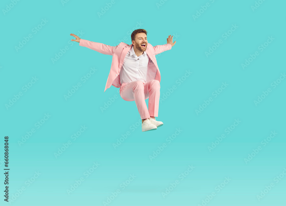Funny guy with unshaven beard wearing stylish bright pink suit jumping high isolated on blue turquoise background. Portrait of a happy young excited man having fun in studio. People emotions concept.