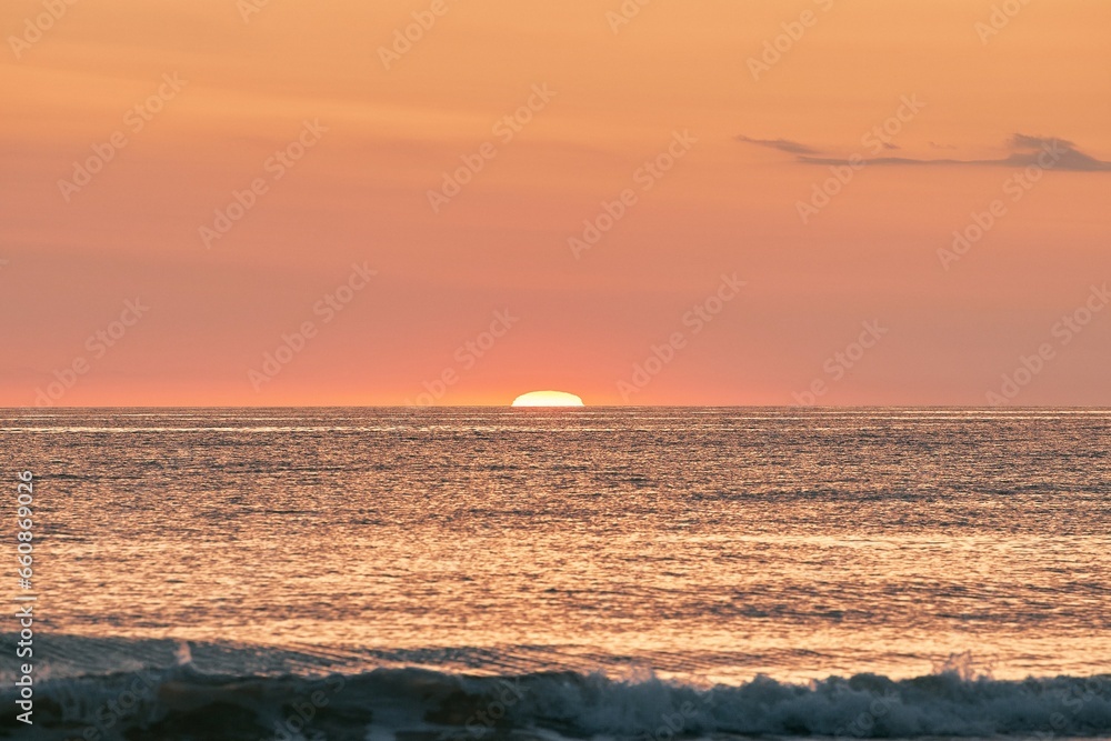 The glowing sun sinking on the horizon of the sea or ocean The glowing sun sinking on the horizon of the sea or ocean