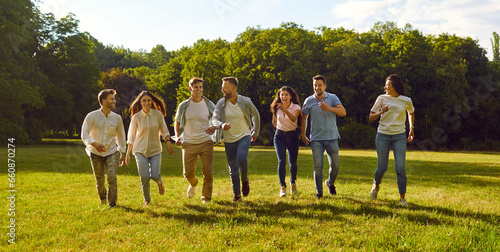 Group of a young people friends walking in the summer park. Happy people girls and boys having fun and running outdoors. Smiling students in casual clothes spending time together on the lawn. Banner.