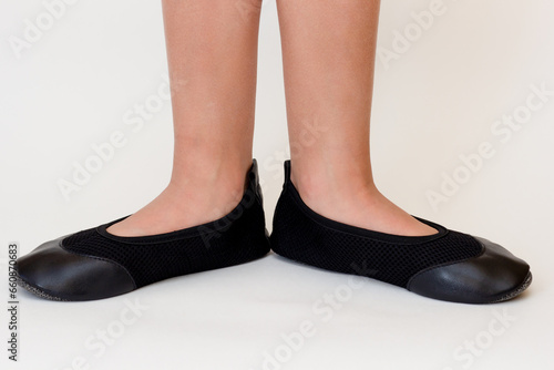 Cropped child legs in black leather ballet shoes on white background