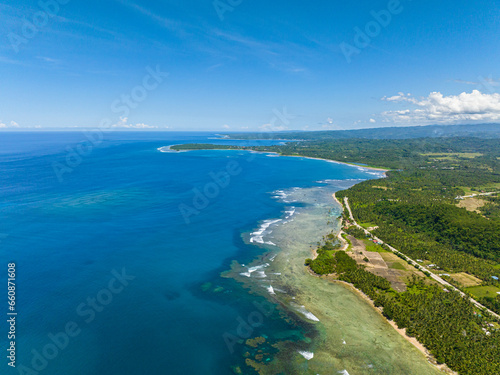 Tropical island with white sand shoreline and beautiful waves in coast. Blue skies and clouds. Mindanao, Philippines.