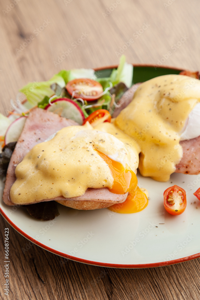 Eggs Benedict, breakfast and brunch, made from poached egg, English muffin,  ham, bacon, Hollandaise sauce and mixed salad 