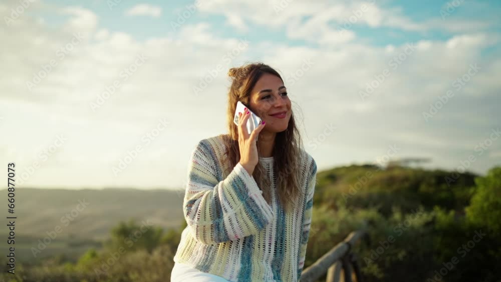 Attractive young woman making a cell phone call while smiling with sunset behind her. Attractive young woman making a cell phone call while smiling with sunset behind her.
