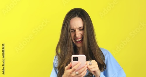 happy young casual woman in blue sweater reading and scrolling social media screaming and pointing finger to screen, laughing and show thumb up gesturing on yellow background