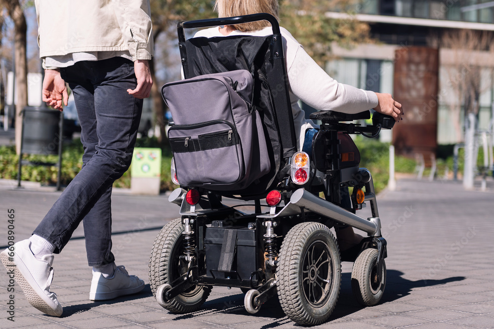 cropped rear view of an unrecognizable woman using wheelchair with a man taking a walk by the city, concept of friendship and diversity cropped rear view of an unrecognizable woman using wheelchair with a man taking a walk by the city, concept of friendship and diversity