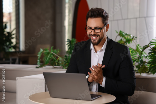Happy young man with laptop at table in office