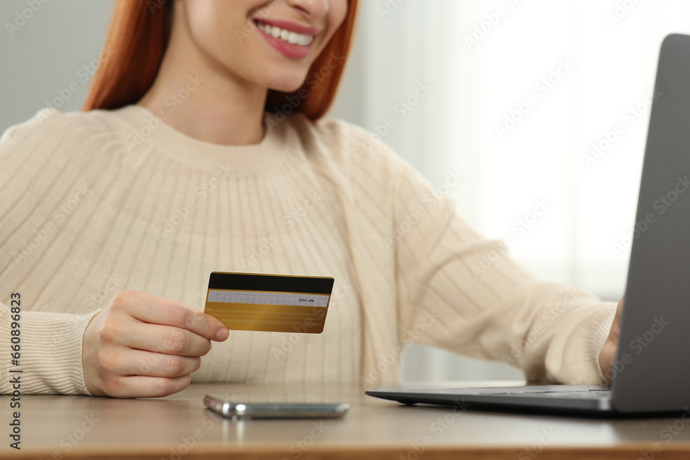 Woman with credit card using laptop for online shopping at wooden table indoors, closeup Woman with credit card using laptop for online shopping at wooden table indoors, closeup
