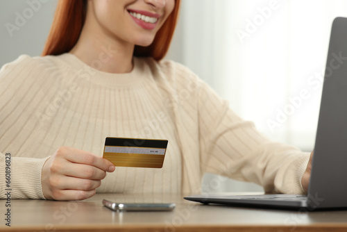 Woman with credit card using laptop for online shopping at wooden table indoors, closeup