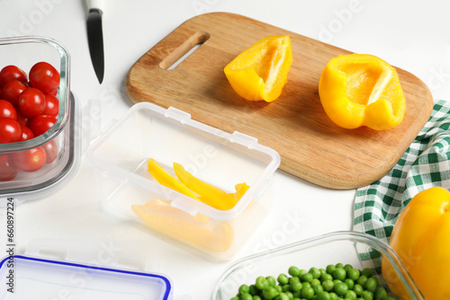 Wooden board with cut bell pepper and containers with fresh products on white table. Food storage