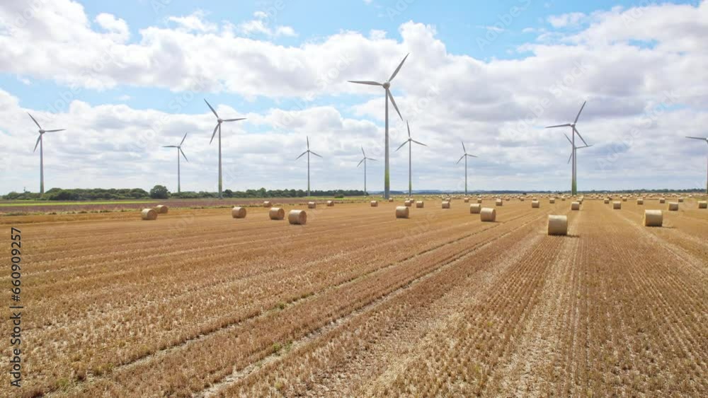 High above, the camera records the tranquil scene of wind turbines spinning gracefully in a Lincolnshire farmer's field, recently harvested and adorned with golden hay bales. High above, the camera records the tranquil scene of wind turbines spinning gracefully in a Lincolnshire farmer's field, recently harvested and adorned with golden hay bales.