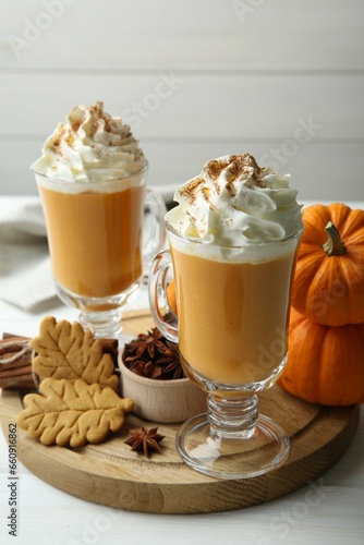 Tasty pumpkin latte with whipped cream in glasses, spices and cookies on white wooden table