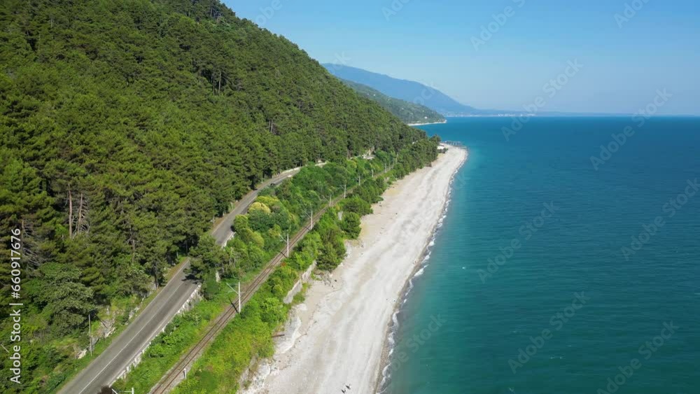 Aerial view of empty tropical beach and blue sea water. Drone footage of the coastal road, trees on the shore and the blue sea in Abkhazia Aerial view of empty tropical beach and blue sea water. Drone footage of the coastal road, trees on the shore and the blue sea in Abkhazia